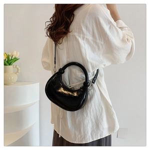 Polished black crescent bag in glossy patent leather styled on a model's shoulder