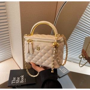 Detail view of beige quilted bucket bag with gold arc metal handle and flower clasp