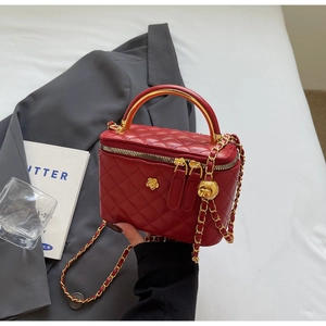 Macro shot of red quilted vanity bag featuring gold metal handle and chain with ball charm