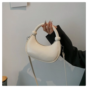 Chic cream semi-circle handbag shown with elegant metal buckle and long shoulder strap