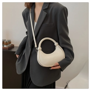 Chic cream half-moon handbag shown on model with stylish dark grey blazer and white top