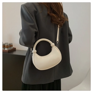 Detail of cream half-moon handbag with knot handle worn by a model in a gray suit