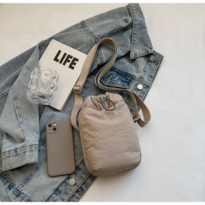 Top view of beige drawstring nylon crossbody bag on a blue denim jacket and book