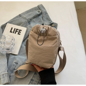 Detail of beige nylon drawstring bag featuring adjustable cords and wide shoulder strap