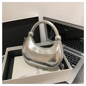 Detail of silver crescent handbag with mirror finish, metallic texture and round handle