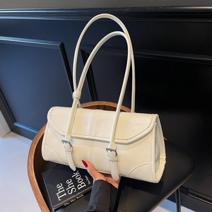 Minimalist cream white baguette bag with silver buckle straps on a black leather chair