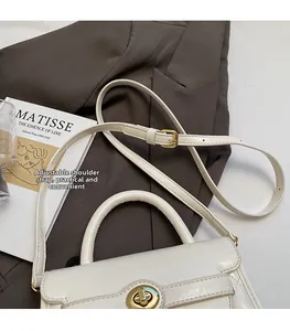 Dettaglio borsa in pelle crema con tracolla regolabile su blazer e libro d'arte