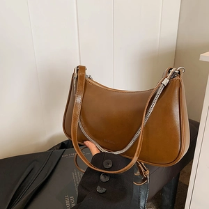 Brown leather crescent shoulder bag with silver chain and dual straps in a warm setting