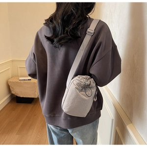 Detail of a grey drawstring nylon bucket bag with adjustable wide strap on model