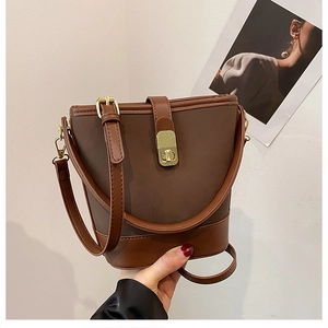 Detail of a brown two-tone bucket bag with gold hardware lock and adjustable straps