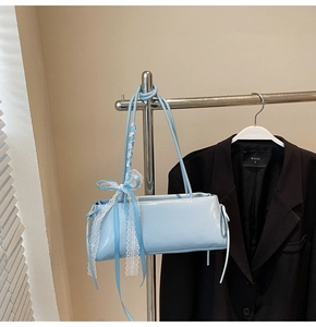 Close-up of light blue baguette bag featuring a lace bow accent on a stylish hanger
