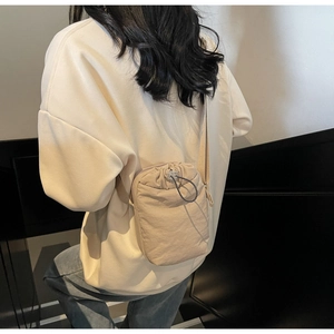 Detail view of beige nylon drawstring mini crossbody bag on model with stairs background