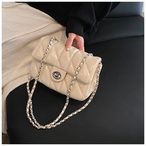 Detail of cream quilted crossbody bag featuring silver chain strap and metal turn-lock