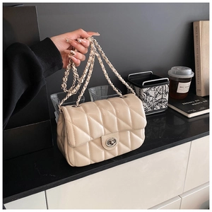 Detail of light beige quilted crossbody bag featuring silver chain strap and turn-lock closure