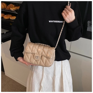 Detail of beige quilted crossbody bag with silver chain strap and metal turn-lock closure