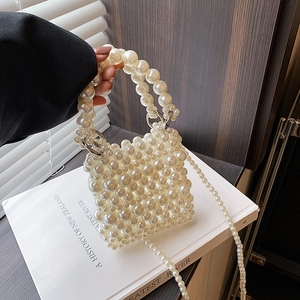 Elegant ivory pearl beaded handbag with top handle and crossbody chain on white books