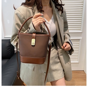 Close-up of a brown leather bucket bag with gold metal clasp on a stylish model