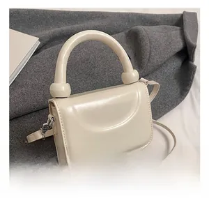 Détail d'un sac à main crème avec poignée en anneau et bille métallique décorative