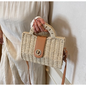 Detail of handwoven straw handbag featuring a brown leather flap and metal ring twist lock