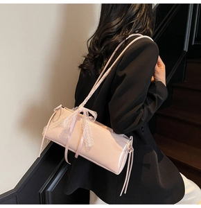 Pink patent leather pillow bag with white lace bow detail shown on a model's shoulder