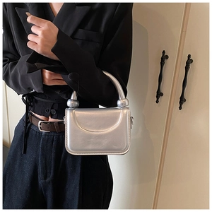 Détail d'un sac à main argenté métallisé avec poignée cylindrique et rabat minimaliste chic