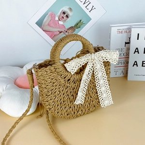 Detail of hand-woven straw bag featuring a large white lace bow and drawstring closure