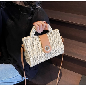 Detail of handwoven beige straw bag featuring a brown faux leather flap and metal clasp