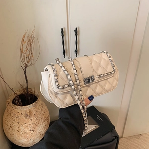 Chic beige quilted crossbody chain bag held by hand in a minimalist home setting