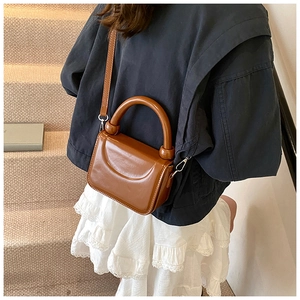 Sac carré en similicuir marron porté avec une veste bleue et une jupe plissée blanche