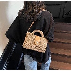 Detailed view of handmade woven straw bag with brown leather handle and metal clasp closure