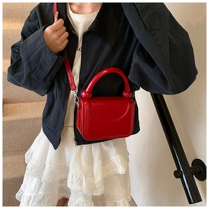 Détail du petit sac carré rouge brillant avec une poignée incurvée unique et des détails sphériques