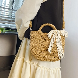 Detail of woven straw bag with white lace bow decoration and long shoulder strap