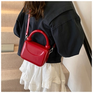 Détail du mini sac carré en cuir verni rouge avec poignée ronde sur escalier neutre