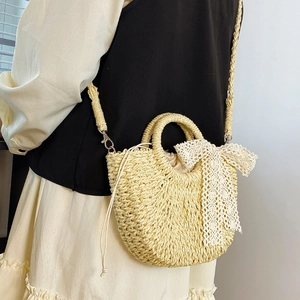 Detail of hand-woven straw bag featuring a decorative white lace ribbon bow accent