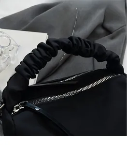 Close-up of minimalist black nylon handbag with scrunchie handle and silver zipper detail