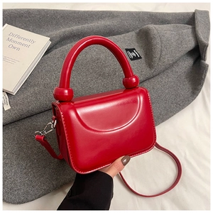 Détail d'un sac bandoulière rouge brillant avec poignée épaisse et garnitures argentées
