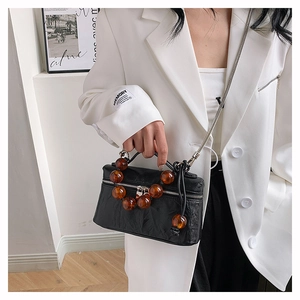 Modèle portant un sac en cuir plissé noir avec perles ambrées et bandoulière chaîne