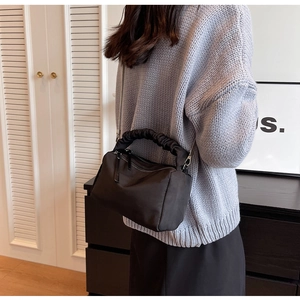 Detail of a black nylon crossbody bag featuring unique ruched handles and double zipper