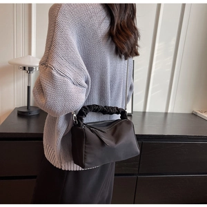 Detail of a black nylon dumpling bag featuring a ruched cloud handle and silver chain strap