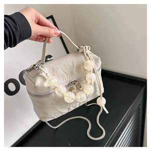Détail du sac à main plissé crème avec poignée perlée et bandoulière tressée