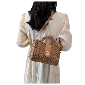 Handmade woven straw handbag with brown leather flap and gold clasp on a female model