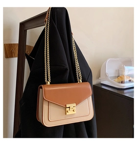 Dettaglio borsa a tracolla bicolore con catena dorata su un blazer nero elegante