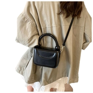 Mini sac à main noir brillant avec poignée et bandoulière porté par un mannequin