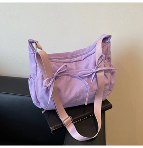 Close-up of light purple nylon bag with bow details on a leather sofa surface