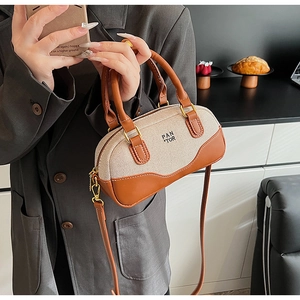 Detail of canvas and brown leather mini bowling bag held by a model in casual blazer