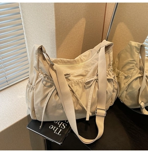 Detail of beige canvas shoulder bag featuring drawstring bow and adjustable fabric strap