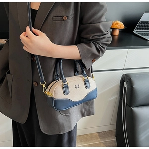 Model showcasing a mini canvas bowling bag with navy leather trim and gold metal hardware