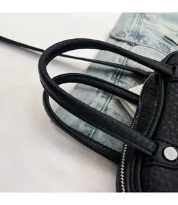 Close-up of black lychee grain leather handbag with round handles and silver zipper
