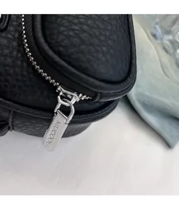Close-up of black lychee leather texture and silver metal zipper with engraved logo