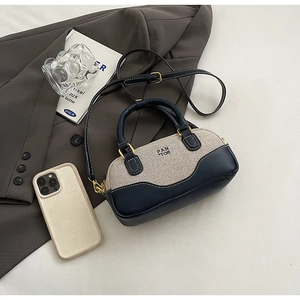 Detail of navy leather and beige canvas bowling bag with gold hardware on a grey blazer